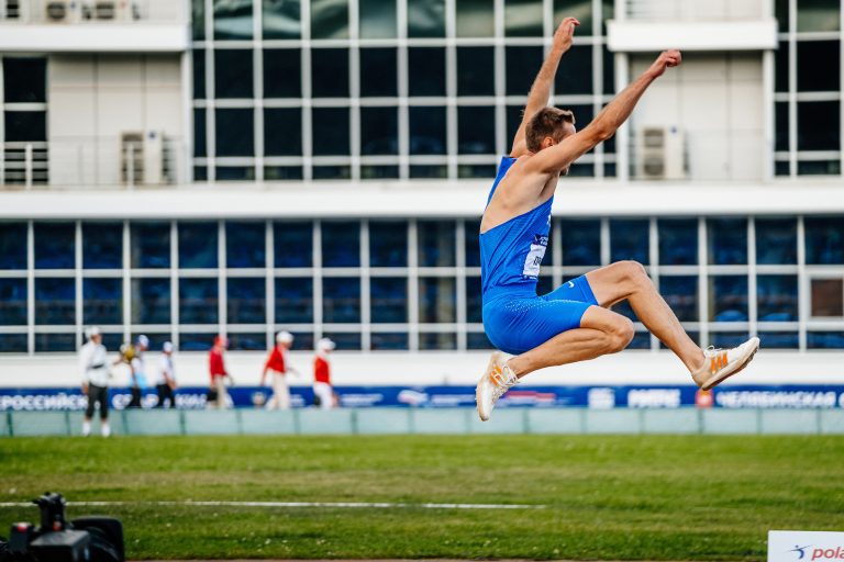 male athlete long jump in competition athletics, spikes shoes for jumping Adidas and tights Nike, sports photo