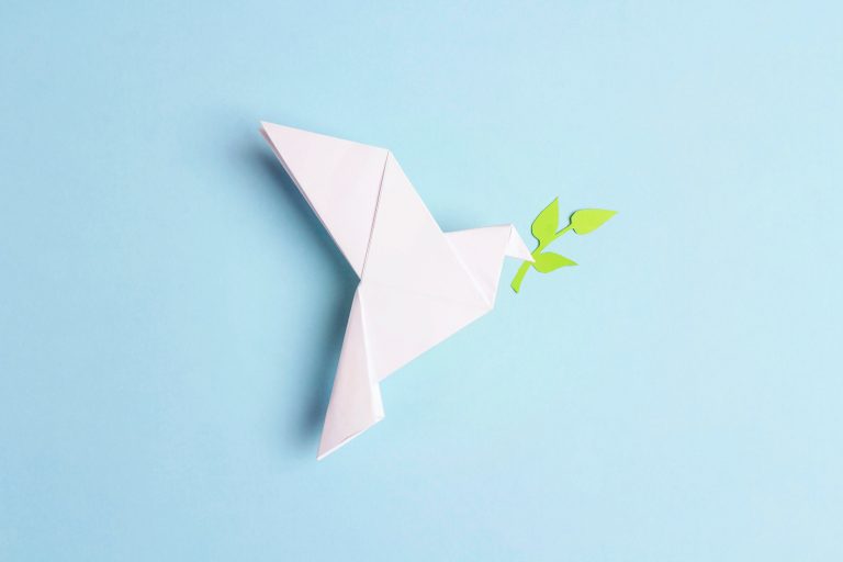 Paper origami dove of peace with olive branch on a blue backgrou