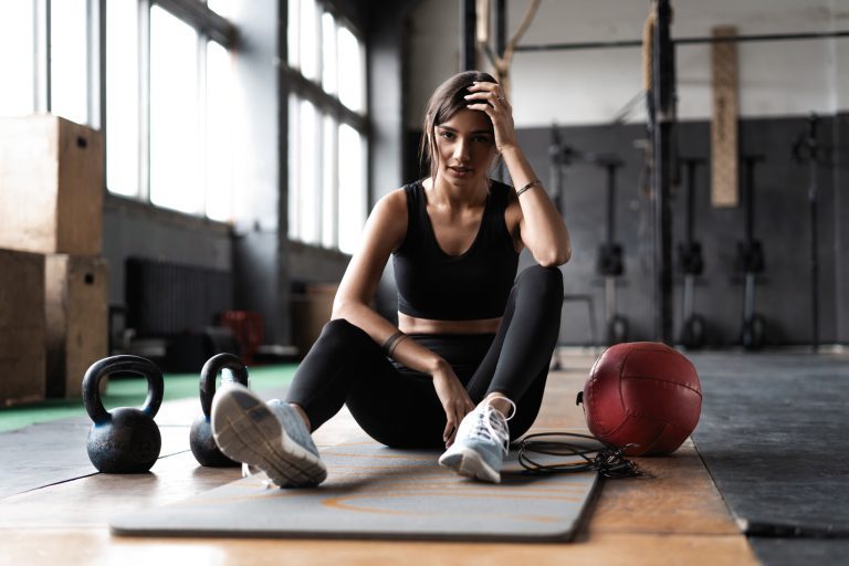 Young woman sitting on floor after her workout and looking down