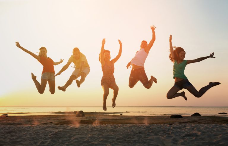 smiling friends dancing and jumping on beach