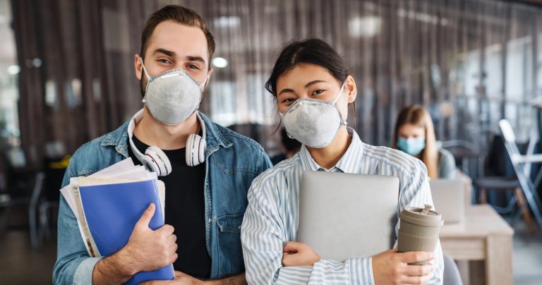 Photo of multinational students in medical masks standing at cla