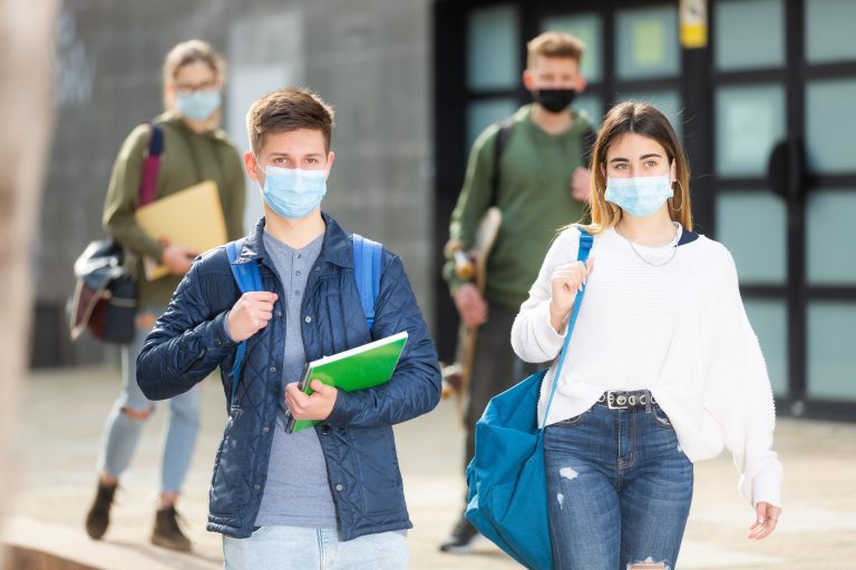 Young girl and guy in protective masks walk along street holding hands