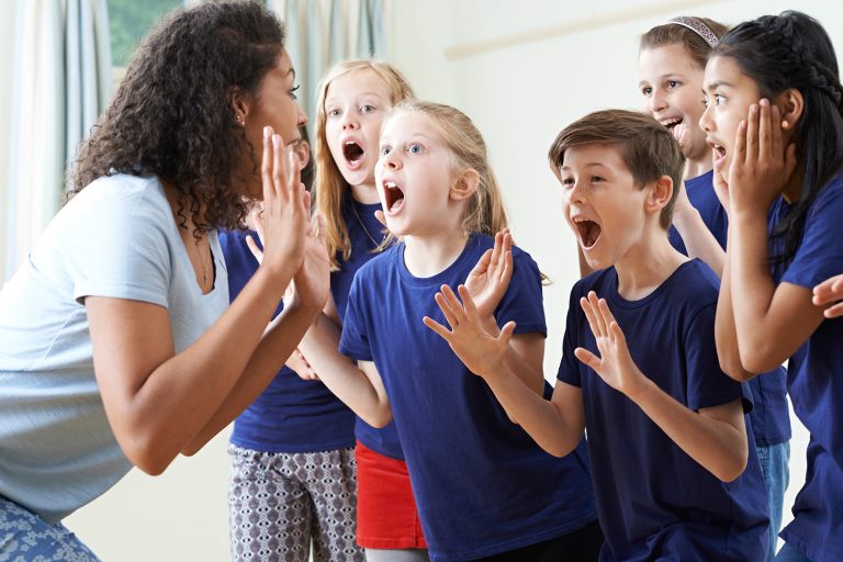 Group Of Children With Teacher Enjoying Drama Class Together